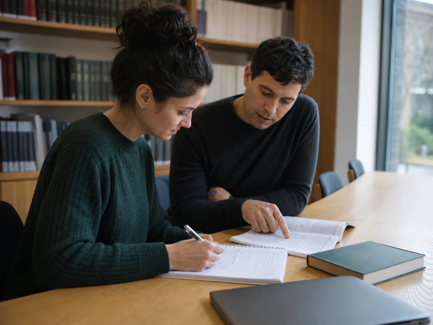 Two adult learners refine academic reading and writing together at a library table