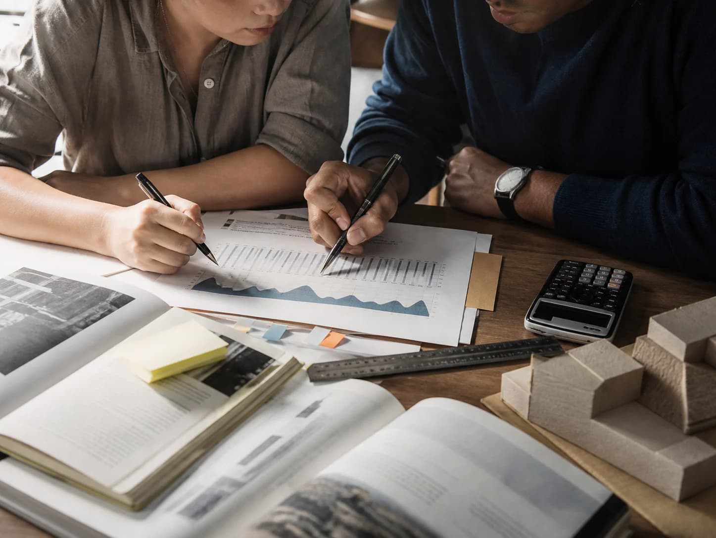 Two adult learners annotate a data chart beside reference books and a geometric model
